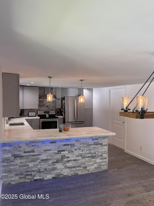 kitchen featuring stainless steel appliances, decorative backsplash, a sink, a peninsula, and dark wood-style floors
