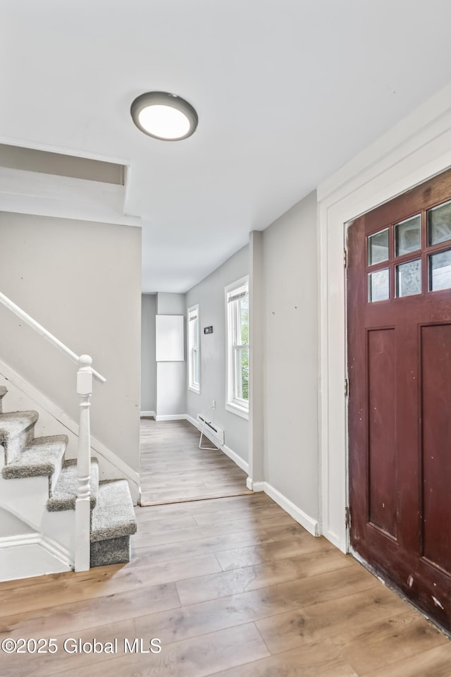 foyer entrance featuring a baseboard radiator, stairway, baseboards, and wood finished floors