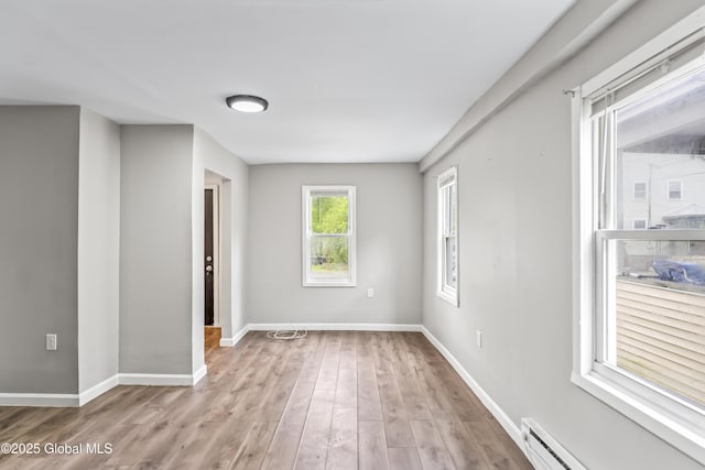 empty room featuring baseboard heating, light wood-type flooring, and baseboards