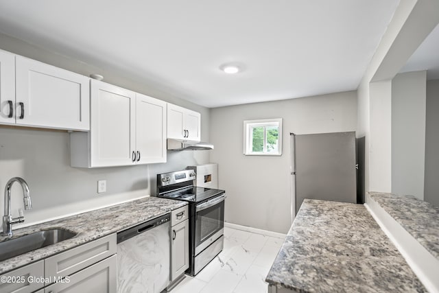 kitchen with appliances with stainless steel finishes, a sink, under cabinet range hood, light marble finish flooring, and white cabinetry