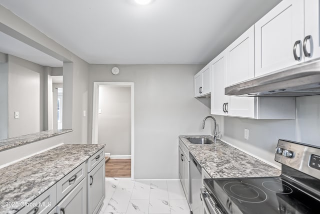 kitchen with appliances with stainless steel finishes, under cabinet range hood, a sink, baseboards, and light marble finish flooring
