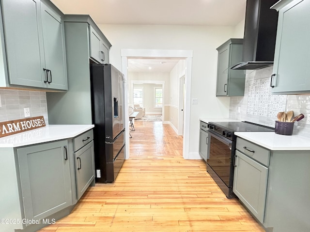 354 Mohawk Ave, Scotia, NY 12302 - kitchen featuring stainless steel fridge, wall chimney range hood, black / electric stove, light countertops, and light wood-style flooring