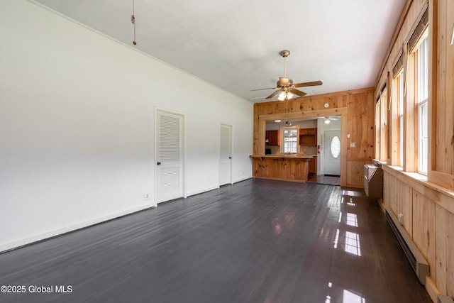 1301 State Route 313, Cambridge, NY 12816 - unfurnished living room with a baseboard heating unit, dark wood-style flooring, wooden walls, a ceiling fan, and baseboards