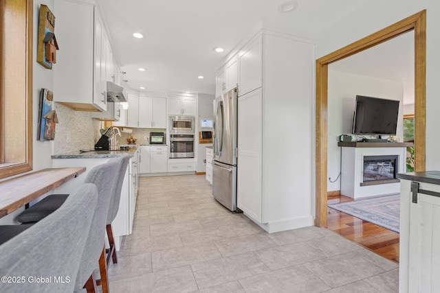 6175 Hawes Rd, Guilderland, NY 12009 - kitchen featuring stainless steel appliances, a glass covered fireplace, white cabinetry, decorative backsplash, and recessed lighting