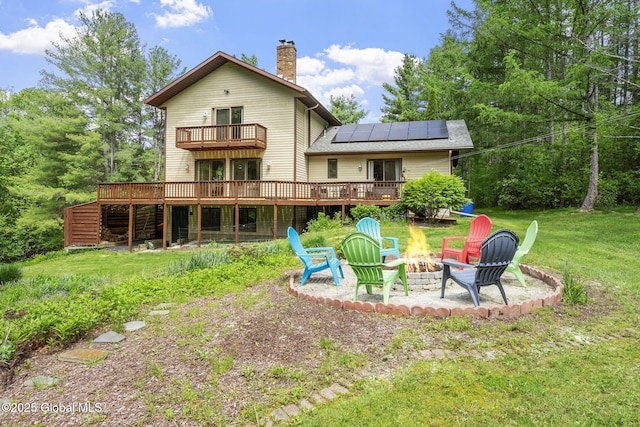 6175 Hawes Rd, Guilderland, NY 12009 - back of property featuring a fire pit, a deck, roof mounted solar panels, a chimney, and a lawn