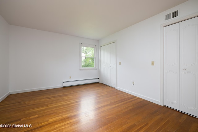 184 Main St, South Glens Falls, NY 12803 - unfurnished bedroom featuring a baseboard heating unit, two closets, wood finished floors, and baseboards