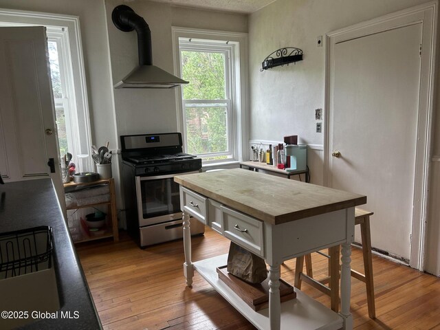 281 10th St, Troy, NY 12180 - kitchen featuring stainless steel gas stove, wall chimney range hood, butcher block countertops, light wood finished floors, and white cabinets