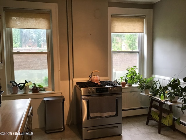 281 10th St, Troy, NY 12180 - kitchen featuring stainless steel gas range oven, light tile patterned floors, a baseboard heating unit, and a wainscoted wall