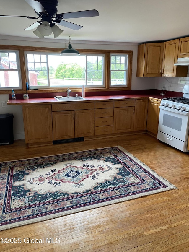 162 Garnet Lake Rd, Thurman, NY 12885 - kitchen with white gas range, wood finished floors, a sink, under cabinet range hood, and brown cabinetry