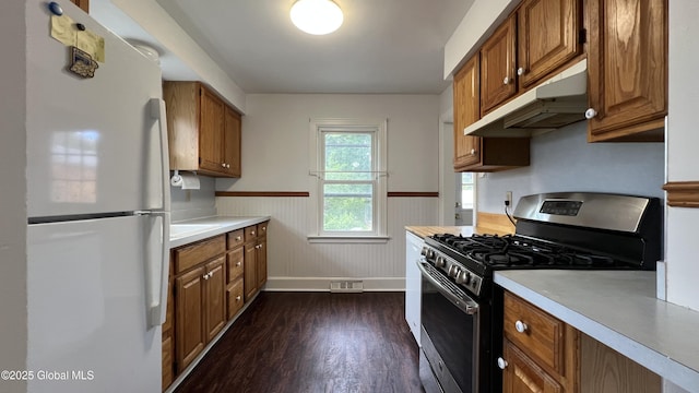 209 Hudson Ave E, East Greenbush, NY 12144 - kitchen featuring freestanding refrigerator, stainless steel range with gas stovetop, under cabinet range hood, wainscoting, and brown cabinetry