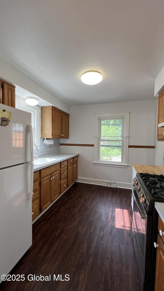 209 Hudson Ave E, East Greenbush, NY 12144 - kitchen featuring freestanding refrigerator, a wainscoted wall, black gas range, dark wood-style floors, and brown cabinetry