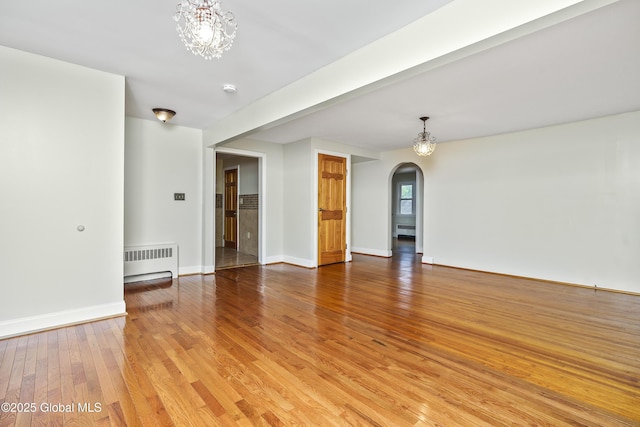 5 Brigadier St, Colonie, NY 12205 - unfurnished living room featuring radiator, arched walkways, a chandelier, light wood-style floors, and baseboards