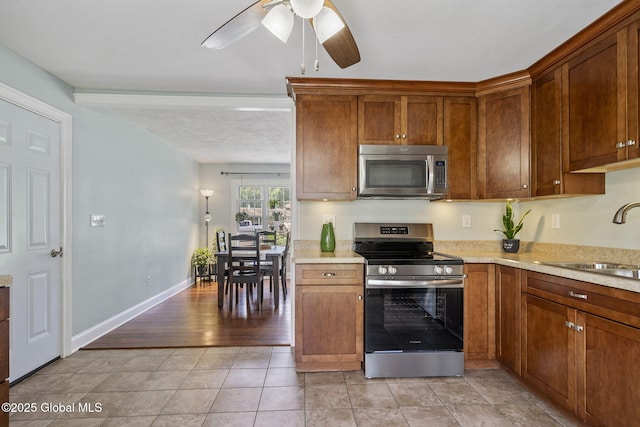 11 Thatcher Dr, Altamont, NY 12009 - kitchen with appliances with stainless steel finishes, a ceiling fan, light countertops, light tile patterned floors, and brown cabinetry