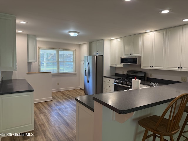 12 Graves St, Glens Falls, NY 12801 - kitchen featuring appliances with stainless steel finishes, light wood finished floors, a breakfast bar, a peninsula, and dark countertops