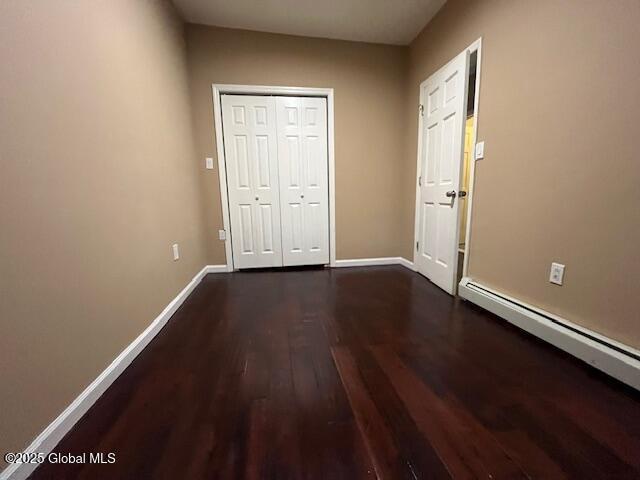 201 10th St, Troy, NY 12180 - unfurnished bedroom featuring dark wood-style flooring, baseboard heating, baseboards, and a closet
