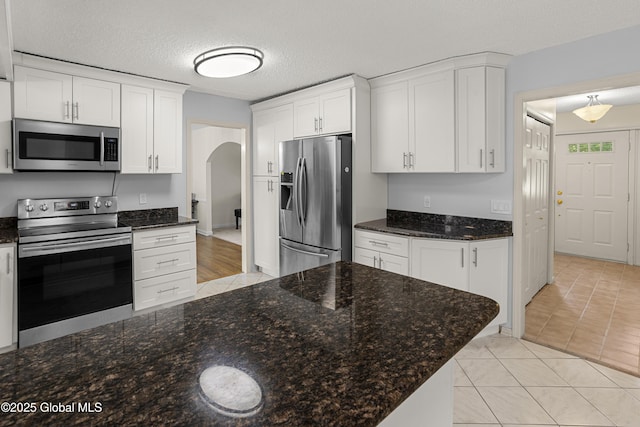 228 Vincenza Ln, Guilderland, NY 12303 - kitchen featuring appliances with stainless steel finishes, arched walkways, white cabinets, dark stone countertops, and light tile patterned flooring