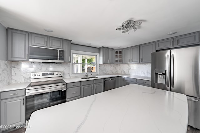 7116 Fuller Station Rd, Schenectady, NY 12303 - kitchen with gray cabinets, stainless steel appliances, a sink, decorative backsplash, and glass insert cabinets