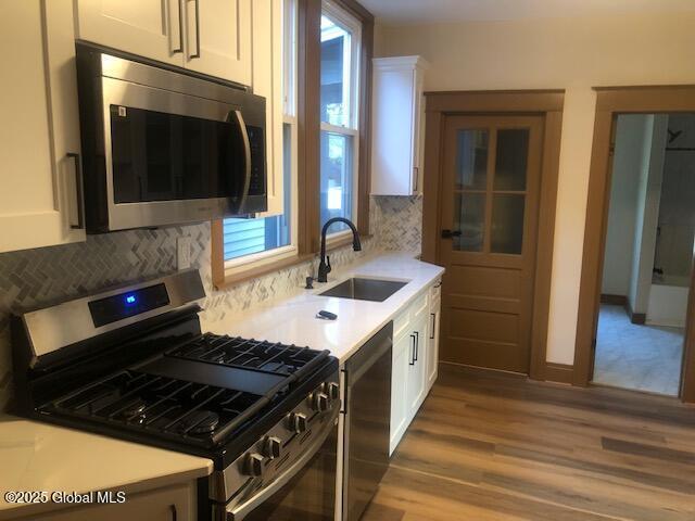 50 Mapleridge Ave, Albany, NY 12209 - kitchen featuring stainless steel appliances, a sink, white cabinets, wood finished floors, and decorative backsplash