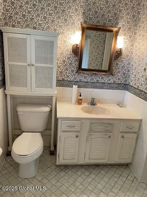 2070 Grand Blvd, Niskayuna, NY 12309 - bathroom with wallpapered walls, toilet, vanity, wainscoting, and tile walls