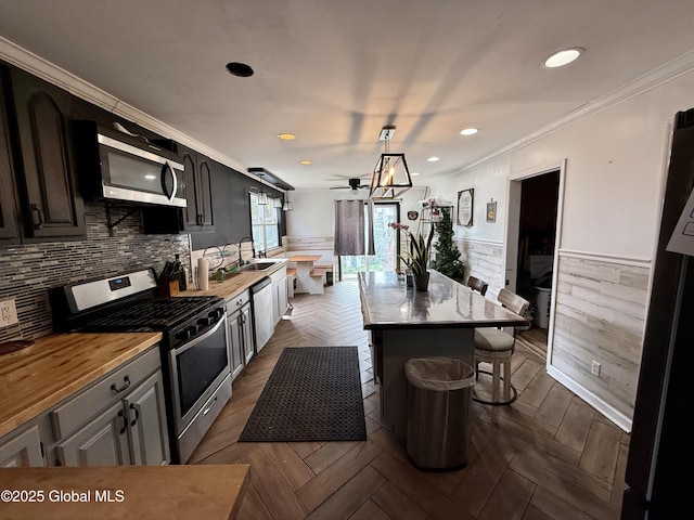 243 N Perry St, Johnstown, NY 12095 - kitchen with appliances with stainless steel finishes, a wainscoted wall, a breakfast bar, ornamental molding, and a kitchen island