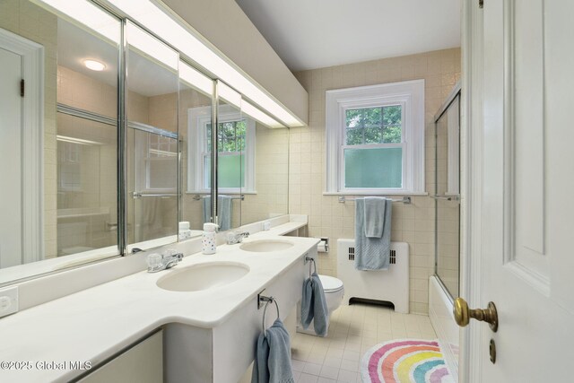 20 Darroch Rd, Bethlehem, NY 12054 - full bath featuring radiator heating unit, tile patterned floors, double vanity, tile walls, and bath / shower combo with glass door