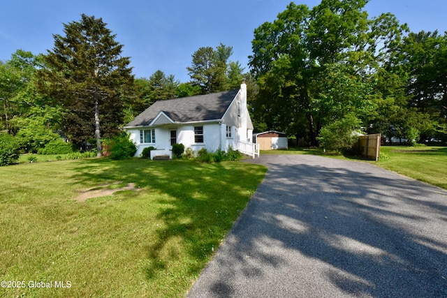 102 Willow St, Guilderland, NY 12084 - view of front facade with asphalt driveway, a front yard, a chimney, and an outdoor structure