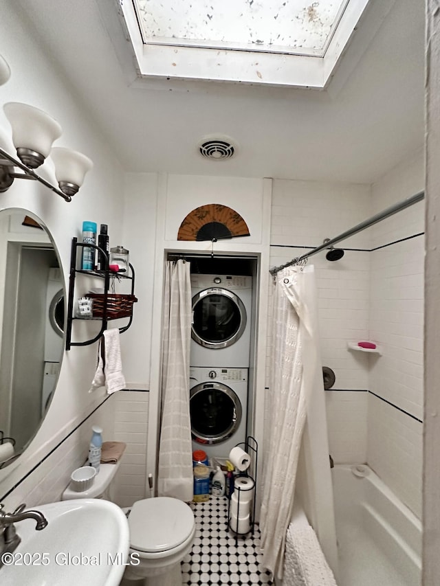 369 Madison Ave, Albany, NY 12210 - bathroom featuring a skylight, stacked washing machine and dryer, a sink, shower / bathtub combination with curtain, and toilet