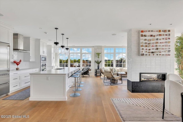 268 Broadway Unit 607, Saratoga Springs, Inside, NY 12866 - kitchen with wall chimney exhaust hood, open floor plan, a breakfast bar, light wood-style floors, and light countertops