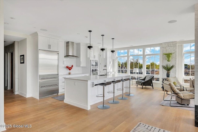 268 Broadway Unit 607, Saratoga Springs, Inside, NY 12866 - kitchen featuring wall chimney exhaust hood, built in appliances, light wood finished floors, a breakfast bar area, and recessed lighting