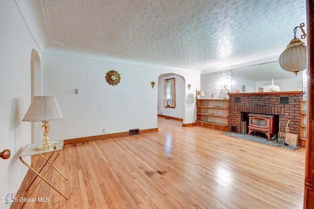 55 Crescent Ave, Amsterdam, NY 12010 - unfurnished living room featuring arched walkways, a wood stove, a textured ceiling, wood finished floors, and baseboards
