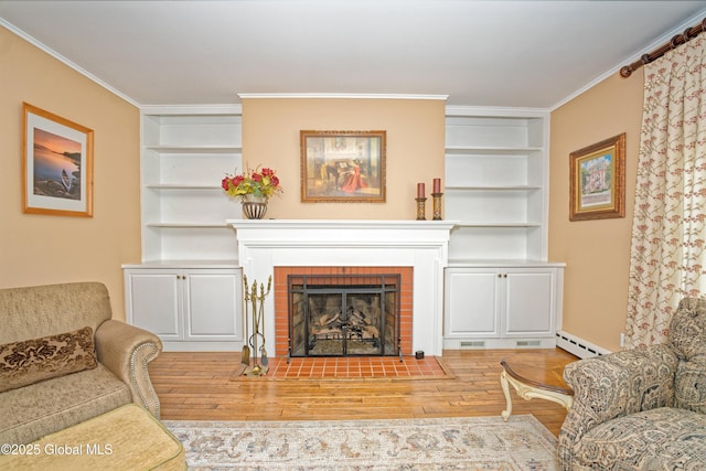 805 Karenwald Ln, Schenectady, NY 12309 - living room with built in shelves, a baseboard heating unit, wood finished floors, a brick fireplace, and crown molding