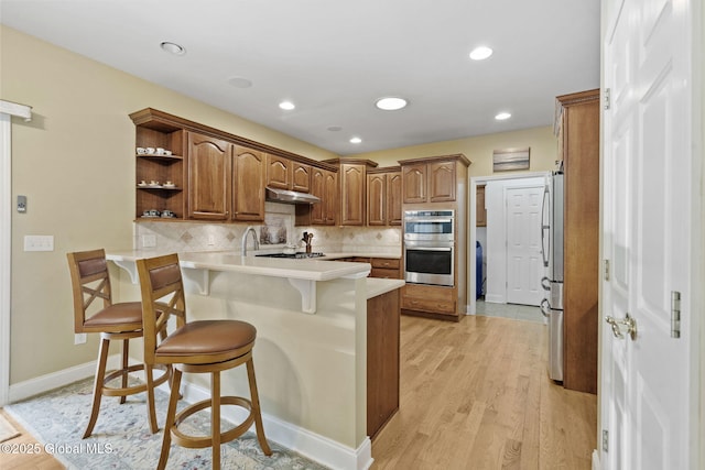 41 Jean Pl, Guilderland, NY 12303 - kitchen featuring appliances with stainless steel finishes, a peninsula, under cabinet range hood, a kitchen breakfast bar, and light countertops