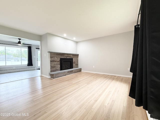 10 Kasper Dr, Colonie, NY 12211 - unfurnished living room with a baseboard heating unit, light wood-type flooring, a stone fireplace, ceiling fan, and baseboards