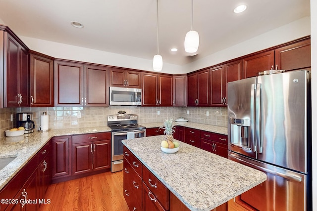 113 Fieldstone Dr, Niskayuna, NY 12304 - kitchen with stainless steel appliances, a kitchen island, decorative light fixtures, backsplash, and light wood-type flooring