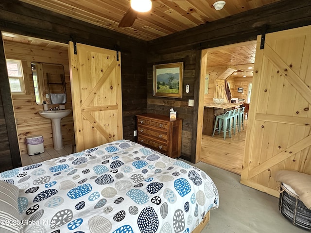 284 Edgemont Rd, Moriah, NY 12960 - bedroom with a barn door, wooden walls, concrete floors, ensuite bath, and wood ceiling