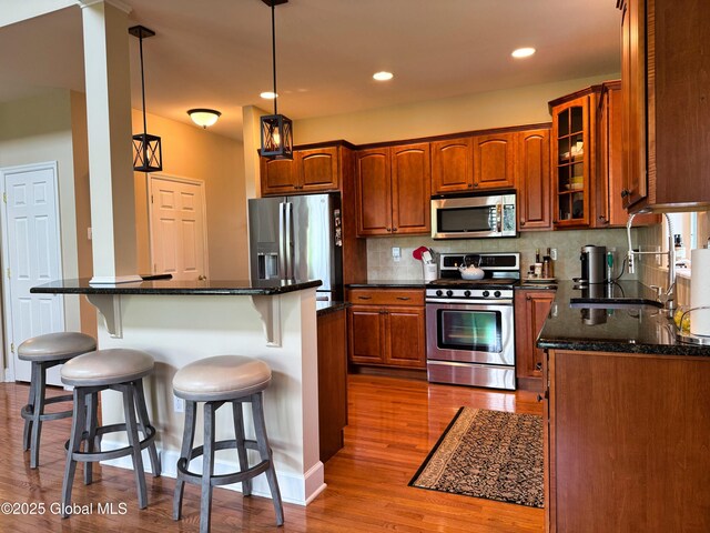 20 Beekman Pl, Queensbury, NY 12804 - kitchen featuring appliances with stainless steel finishes, a kitchen bar, wood finished floors, tasteful backsplash, and glass insert cabinets