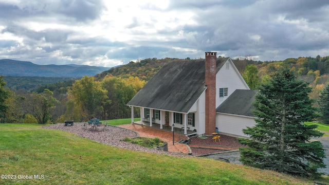 42 Stanton Rd, Jackson, NY 12873 - rear view of property featuring a lawn, covered porch, a chimney, a wooded view, and a mountain view