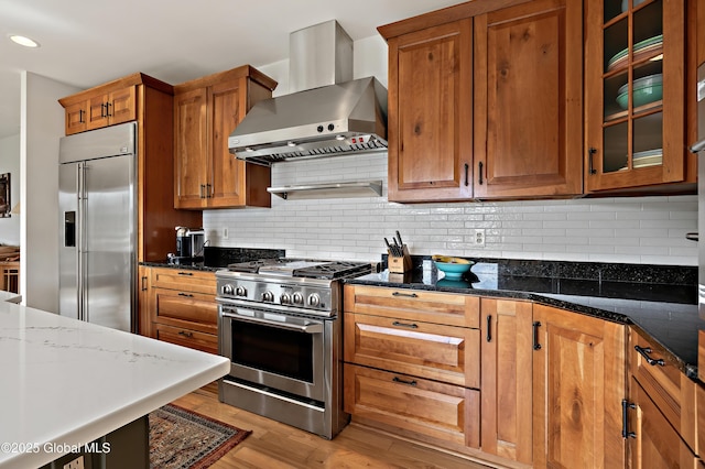 555 Trout Lake Rd, Bolton, NY 12824 - kitchen with wall chimney exhaust hood, high end appliances, brown cabinets, light wood-style floors, and dark stone countertops