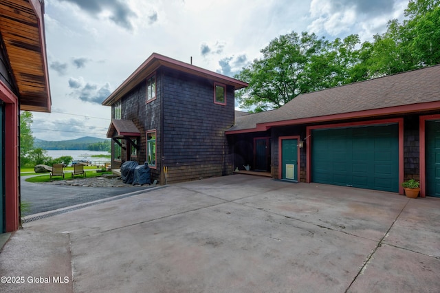 555 Trout Lake Rd, Bolton, NY 12824 - view of side of property featuring concrete driveway, a garage, a water view, and a shingled roof