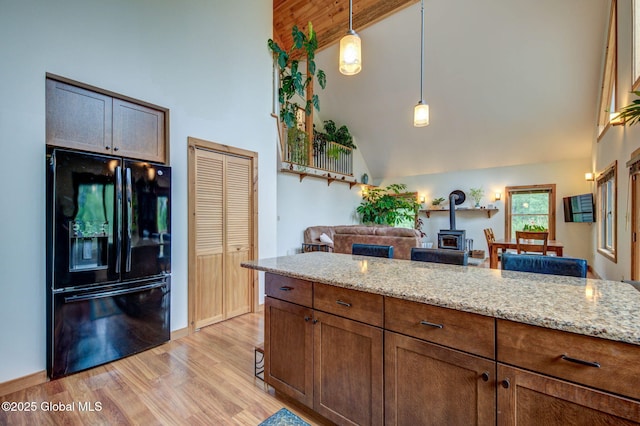 349 Methodist Farm Rd, Sand Lake, NY 12018 - kitchen featuring black fridge with ice dispenser, a wood stove, high vaulted ceiling, light wood-style floors, and light stone countertops