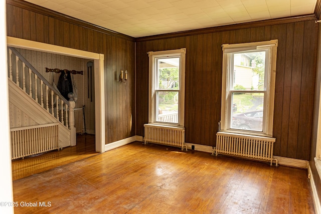 53 Broad St, Catskill, NY 12414 - empty room featuring radiator heating unit, radiator, ornamental molding, stairway, and wooden walls