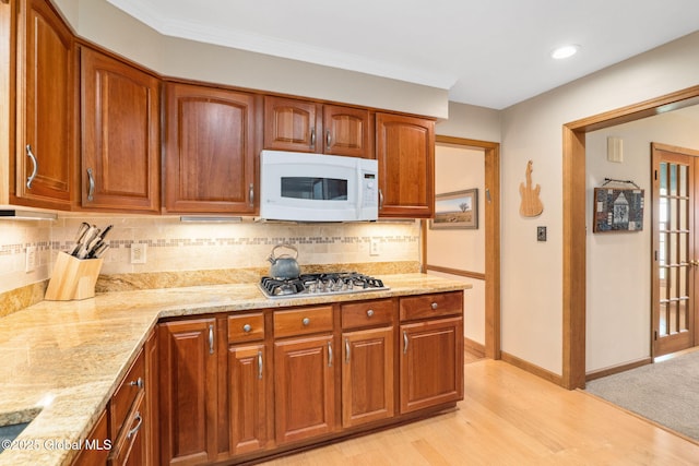 77 Rotterdam Dr, Bethlehem, NY 12077 - kitchen featuring white microwave, stainless steel gas cooktop, light stone counters, light wood-style floors, and backsplash