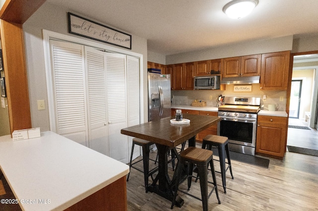 74 Feeder St, Hudson Falls, NY 12839 - kitchen featuring stainless steel appliances, under cabinet range hood, light countertops, light wood-style floors, and brown cabinetry