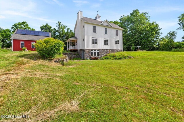 707 Edie Rd, Greenwich, NY 12809 - rear view of property with roof mounted solar panels, a yard, board and batten siding, a chimney, and stone siding