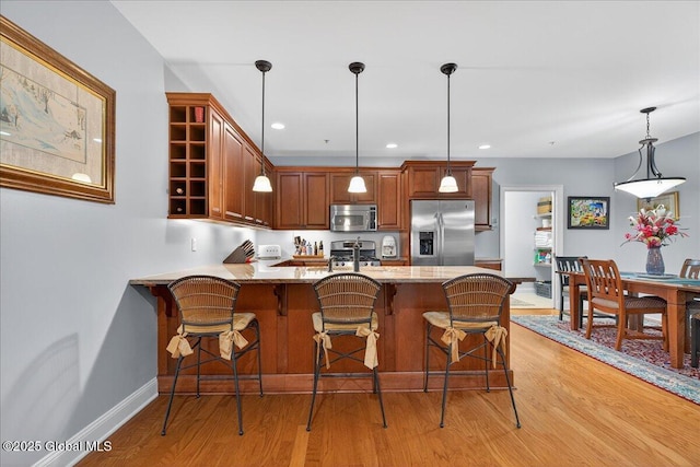 70 Railroad Pl Unit 207, Saratoga Springs, NY 12866 - kitchen with stainless steel appliances, a peninsula, light wood-style flooring, light stone countertops, and hanging light fixtures