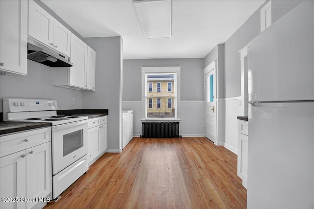 329 E Main St, Amsterdam, NY 12010 - kitchen featuring white appliances, radiator heating unit, under cabinet range hood, dark countertops, and a wainscoted wall