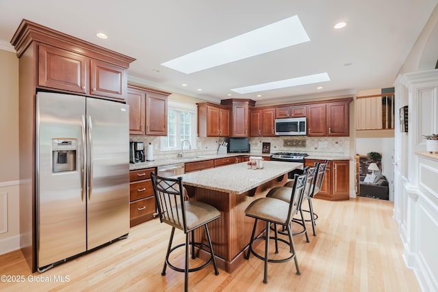 34 Aspen Rd, Colonie, NY 12110 - kitchen with appliances with stainless steel finishes, a skylight, a kitchen breakfast bar, light wood-type flooring, and decorative backsplash