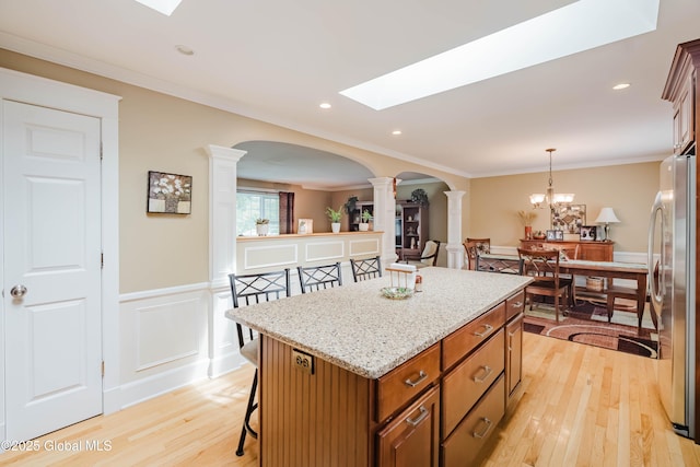 34 Aspen Rd, Colonie, NY 12110 - kitchen with ornate columns, freestanding refrigerator, light wood-style flooring, a kitchen breakfast bar, and brown cabinetry