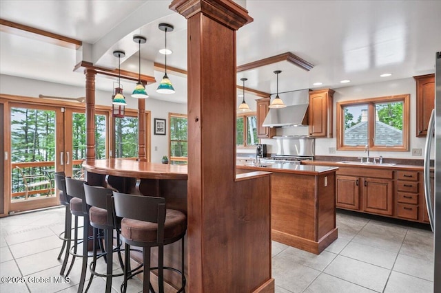 1062 S S Shore Rd, Hadley, NY 12835 - kitchen featuring a kitchen island, wall chimney range hood, light tile patterned floors, brown cabinetry, and a breakfast bar