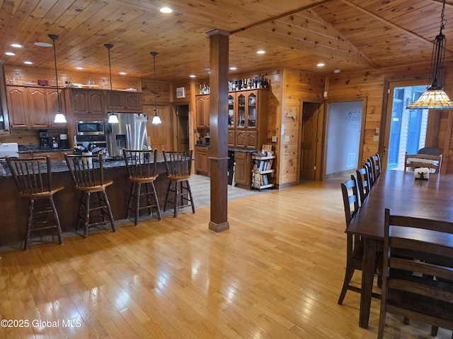 102 Taylor Ct, Mayfield, NY 12117 - kitchen with stainless steel appliances, a breakfast bar area, wooden walls, wood ceiling, and light wood-style floors